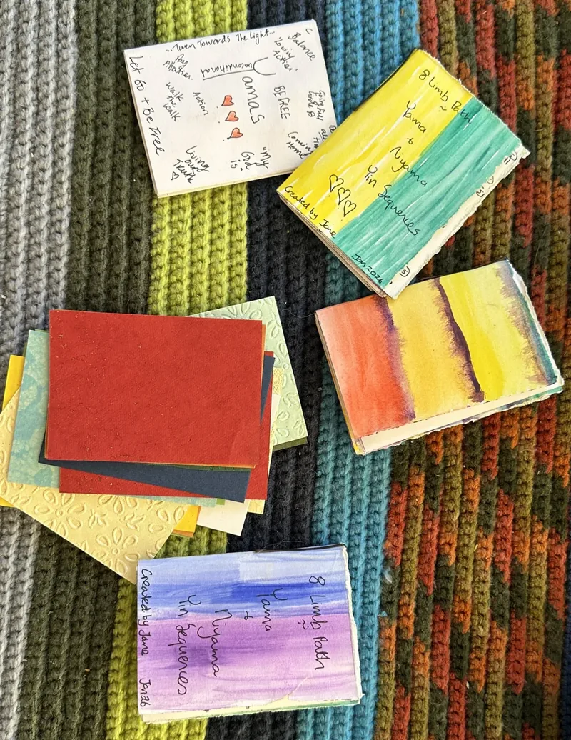 Flat-lay of handmade 8 Limb Path watercolour journals and Yamas notes on a knit blanket